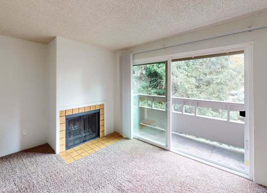 Inviting living room at Heritage Grove Apartments Renton WA with fireplace, large window for natural light, and carpeted flooring.