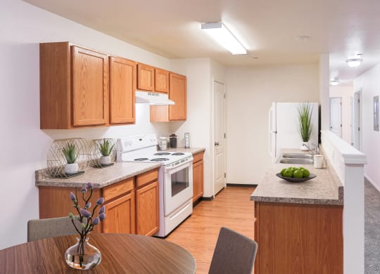 Bright kitchen with honey-colored cabinets and white appliances and faux wood flooring. You can also see down the hallway with white walls and taupe carpet.at Canyon View, Lewiston