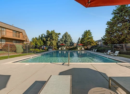 Large swimming pool, lounge chairs, tables, umbrella-covered seating, fenced and surrounded by grass, trees, and bushes.at Castlerock, Wenatchee Washington