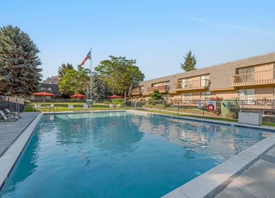 Large swimming pool, lounge chairs, tables, umbrellas, enclosed with fence surrounded by grass and apartments with balconies.at Castlerock, Washington