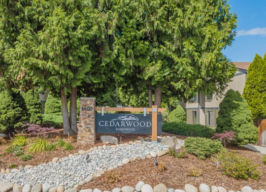 Cedarwood Apartments property sign in landscaped area surrounded by trees..at Cedarwood, Wenatchee, 98801