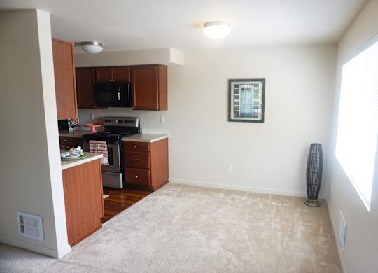 a kitchen and dining area with a carpeted floor and large window at Heritage Grove Apartments in Renton, WA