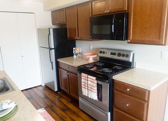 a kitchen with stainless steel appliances and brown wooden cabinets at Heritage Grove Apartments in Renton, WA