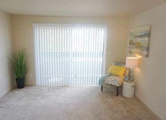 a living room with a large sliding glass door, beige carpet and a chair at Heritage Grove Apartments in Renton, WA