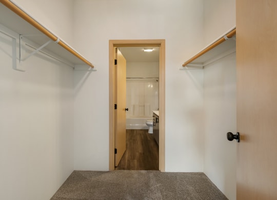 A walk-in closet with custom shelving, taupe carpets, white walls and access to the bathroom.at Shoreline Village, Richland, 99352