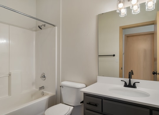 a full bathroom with a vanity sink, white countertops, cabinet storage, a toilet and the shower and bathtub.at Shoreline Village, Washington