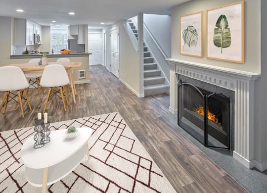 Living room with a gas fireplace, mantle, wood-like floors opens into dining room with stairs to the right next to a hallway.at Edmonds Gateway, Edmonds, WA 98026