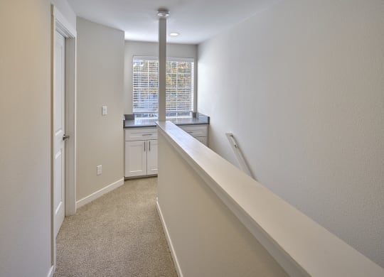 Upstairs carpeted hallway, banister to the right with large window at the top of stairs with counter and cabinets.at Edmonds Gateway, Edmonds, WA