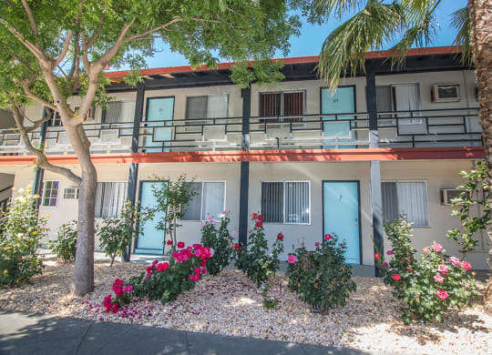 Exterior Building lined with rock garden, pink and red flowers and palm trees at Woodland Village Apartments , Woodland, CA 95695