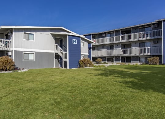 Exterior view of manicured grounds and building, and blue skies in the background at The Lakes Apartments, Moses Lake, WA.