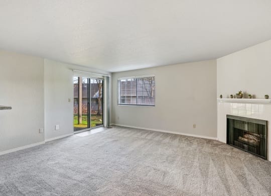 Carpeted living room, gas fireplace, and mantle in the center, with a window and sliding glass doors to a grass lawn.at Capitol Crossing, Olympia, WA