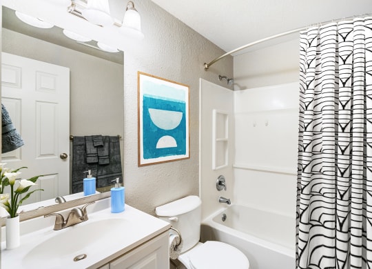 Bathroom with white sink top and below sink cabinets, mirror, toilet, shower with striped curtain.at Capitol Crossing, Olympia