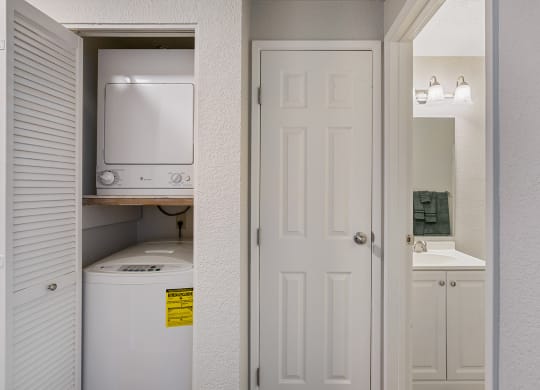 Stacked washer and dryer in shutter door closet to the left of a linen closet with bathroom on the right.at Capitol Crossing, Olympia, WA