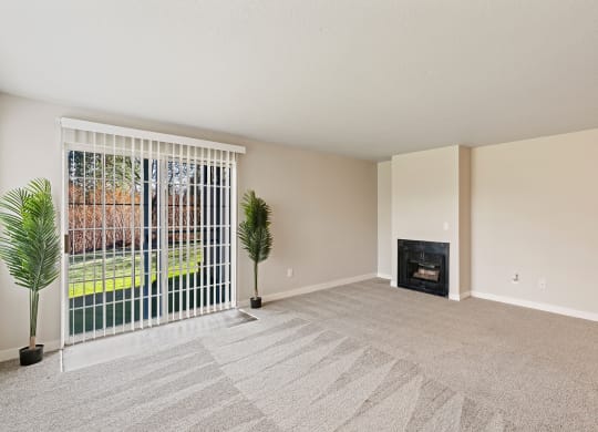 Living room with two plants beside sliding glass doors with panel blinds to grass lawn, and a gas fireplace on back right wall.at Capitol Crossing, Olympia, Washington