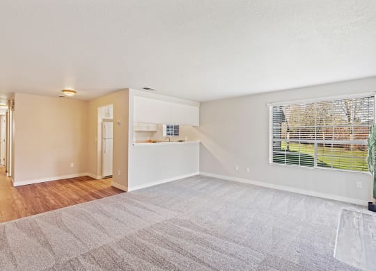 Spacious living room, window with a view of grass and trees, wood floor hallway past kitchen flowing to bedroom on the left.at Capitol Crossing, Olympia, WA