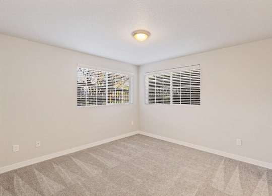 Bedroom corner, gray carpet, windows with white blinds on each wall, views of green trees.at Capitol Crossing, Olympia, Washington