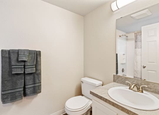 Bathroom with towel rack and staged gray towels, toilet, sink, under sink cabinets, and mirror with overhead lighting.at Capitol Crossing, Olympia, WA 98501