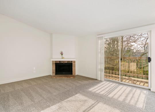 A large carpeted living room with white walls, a fireplace, and sliding glass doors to a private balcony with nature views. at Pointe East, Washington, 98424