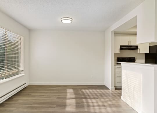 A dining room with white walls, wood flooring, a large window on the left wall, and access to the kitchen on the right side. at Pointe East, Fife, WA, 98424