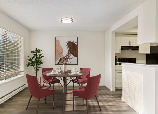 Dining room with white walls, hardwood flooring, a large window on the left wall, and the kitchen to the right. Staged with dining set. at Pointe East, Fife, WA