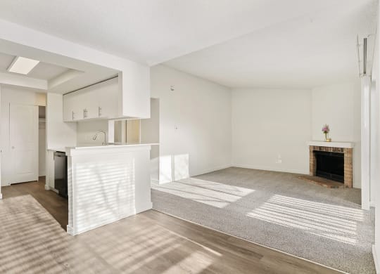 A kitchen with wood flooring, white cabinets, and a breakfast bar opens into a spacious carpeted living room. at Pointe East, Fife, WA