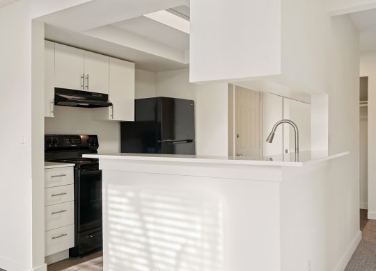 A kitchen with a large l-shaped breakfast bar, white top and bottom cabinets, and upgraded appliances. at Pointe East, Fife, Washington