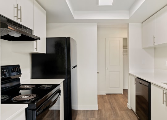 A galley-style kitchen with white cabinets, black appliances, and access to the hallway and hallway closet behind. at Pointe East, Fife, WA, 98424