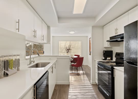 Bright kitchen with hardwood flooring, white top and bottom cabinets, and countertops. There is a dishwasher, sink, oven, stovetop, and fridge from left to right. at Pointe East, Washington, 98424