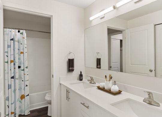 Full bathroom with a double sink vanity and cabinet storage, a large mirror, and a door to the shower and toilet. at Pointe East, Washington, 98424