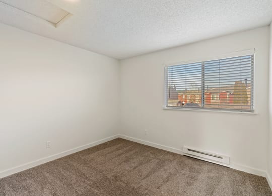 A bedroom with white walls, taupe carpets, a double window with white blinds, and a view on a sunny day. at Pointe East, Fife, Washington