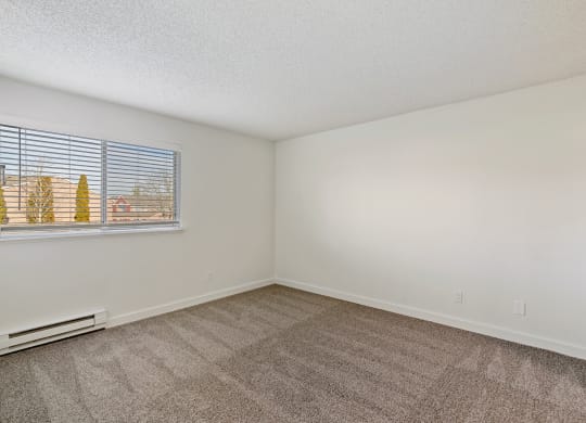 A spacious bedroom with white walls, sunny windows, a heater below the window, and taupe carpets. at Pointe East, Washington, 98424
