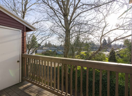 A private apartment balcony with a wood railing looks at trees, bushes, and a grass yard. at Pointe East, Fife, WA, 98424
