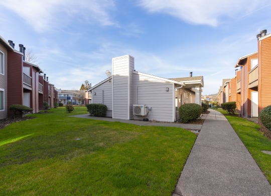 A paved pathway surrounded by green grass leads to apartments on a sunny blue sky day. at Pointe East, Washington, 98424