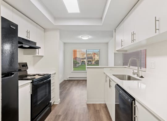 A galley-style kitchen with white countertops and cabinets looks into the dining room with a large window and a view of a grass lawn. at Pointe East, Washington