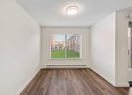 A dining room with white walls, wood flooring, overhead lighting, and an oversized window with a view of a bright green lawn. at Pointe East, Fife, WA, 98424