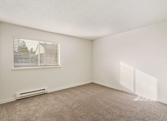 A large bedroom with white walls, taupe carpets, and a sunny window with white blinds. at Pointe East, Fife, Washington