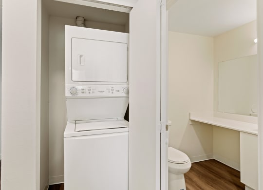 A closet with a white washer and dryer stacked and access to the bathroom on the right. at Pointe East, Washington, 98424
