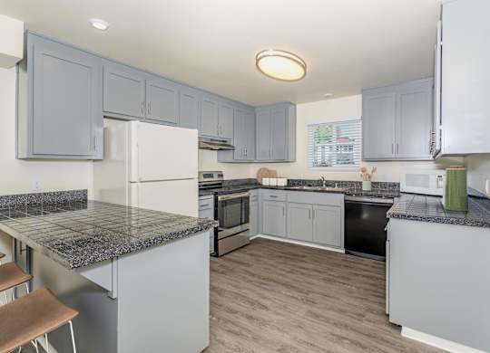 A kitchen with a granite counter top and grey cabinets at Gateway Student Apartments in Chico, CA.