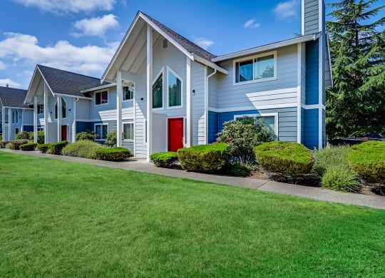 Paved path leading to Hawks Prairie Townhomes, exterior blue accents, and bright green well-maintained landscaping. at Hawks Prairie, Washington