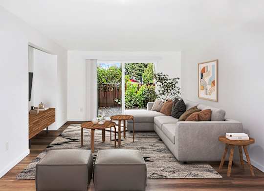 A living room with a grey couch, a wooden coffee table, and a large window with a view of a garden at Heritage Woods Apartments in Renton.
