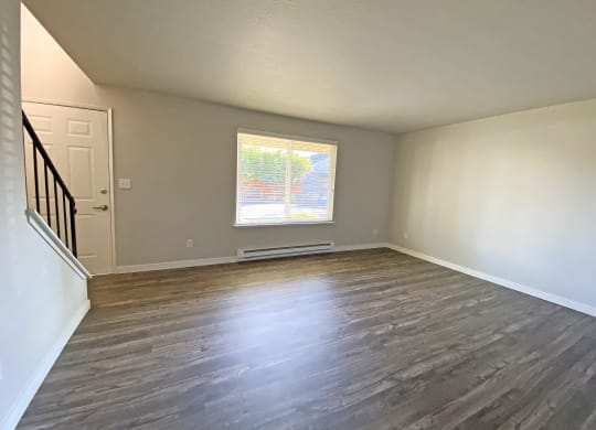 Spacious living room with large window, wood-style flooring, front door, and stairs to the right.at Quilceda Gardens, Washington