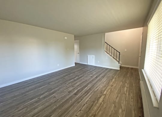 Large living room with faux wood flooring, a large window on the right wall, and an upstairs stairwell on the back wall.at Quilceda Gardens, Marysville, Washington