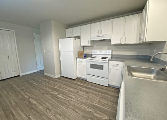 L-shaped kitchen with white appliances, top and bottom cabinets, wood-like flooring, and closet.at Quilceda Gardens, Marysville, WA