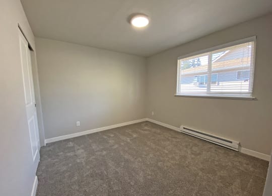 Bedroom with gray carpets, large closet on the left opposite window with white blinds and heater below.at Quilceda Gardens, Marysville, WA 98270