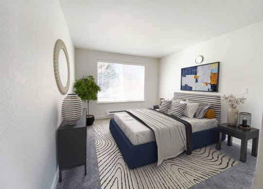 An apartment bedroom with white walls, a large window on the back wall and gray carpet. Staged with a queen-size bed, side tables, a dresser and a rug.at The Trail, Snohomish Washington