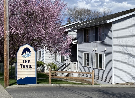 the Trail Apartments sign in front of a white building with a cherry tree in the foreground.at The Trail, Washington