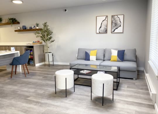 The Trail Apartments lobby with a gray couch, a coffee table, ottoman seating, a mini fridge with drinks and a long table with snacks.at The Trail, Snohomish, 98290