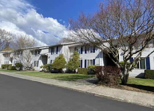 Apartments with grass yards in front, landscaping, trees and a paved walkway. Blue skies are behind the apartments.at The Trail, Snohomish, WA 98290