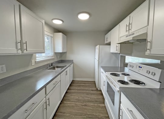 Kitchen with white cabinets, full-size fridge, sink, stovetop, oven, dishwasher, w/ opening looking into living room.at Quilceda Gardens, Marysville