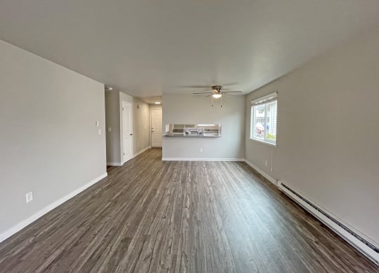 Spacious living room with dining area looking into kitchen with wood-like flooring and oversized window on the right.at Quilceda Gardens, Marysville, WA